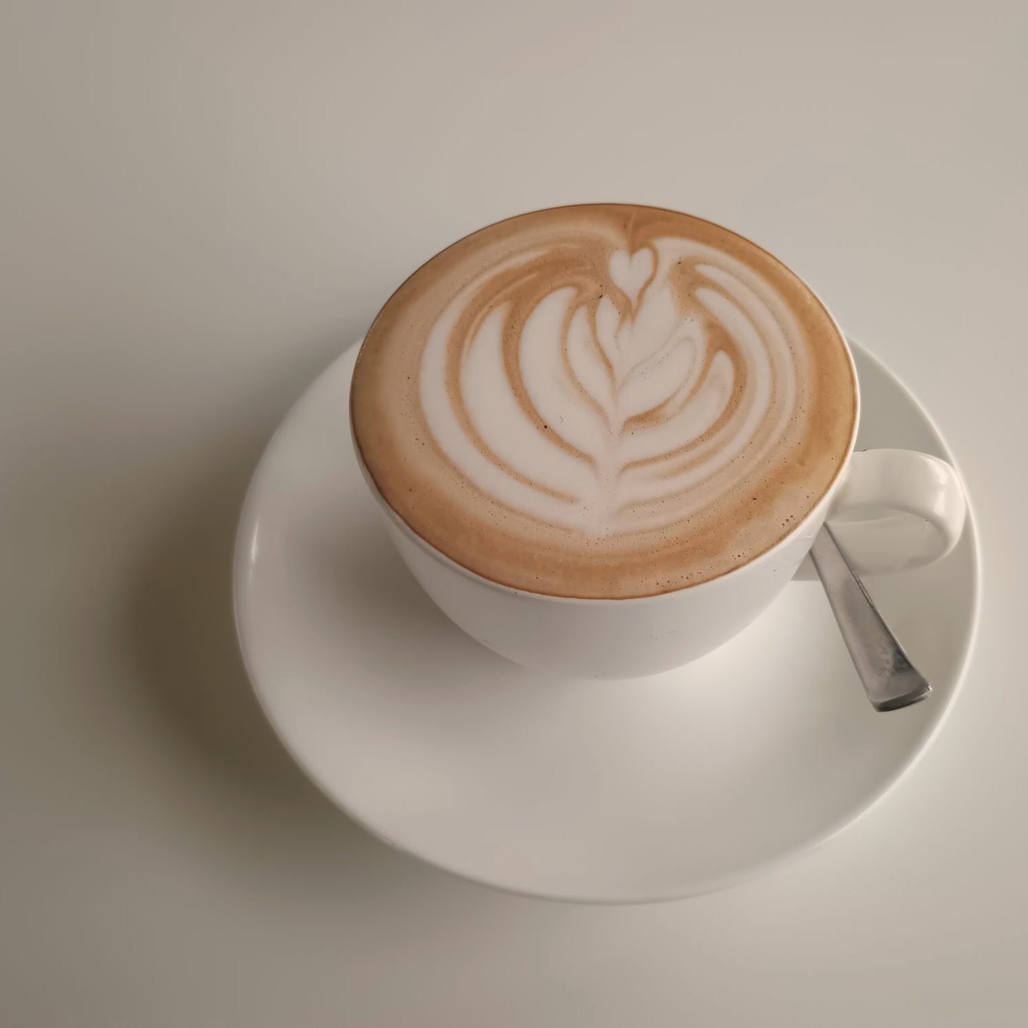 Capuchino con arte latte en una taza blanca sobre su platillo