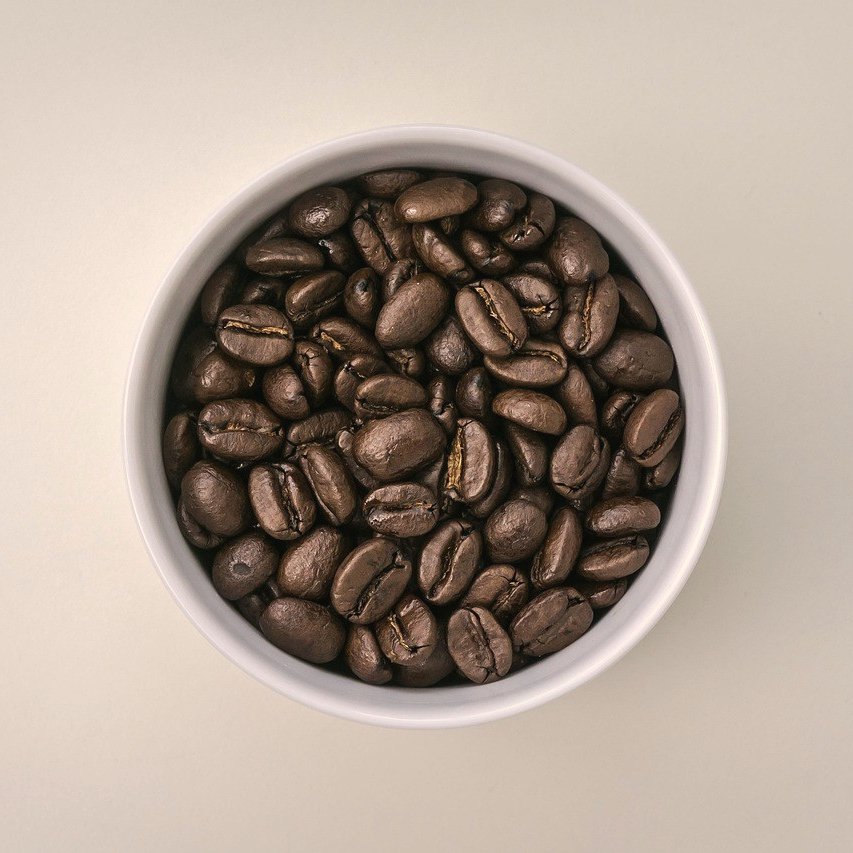 Tazón blanco lleno de granos de café tostado