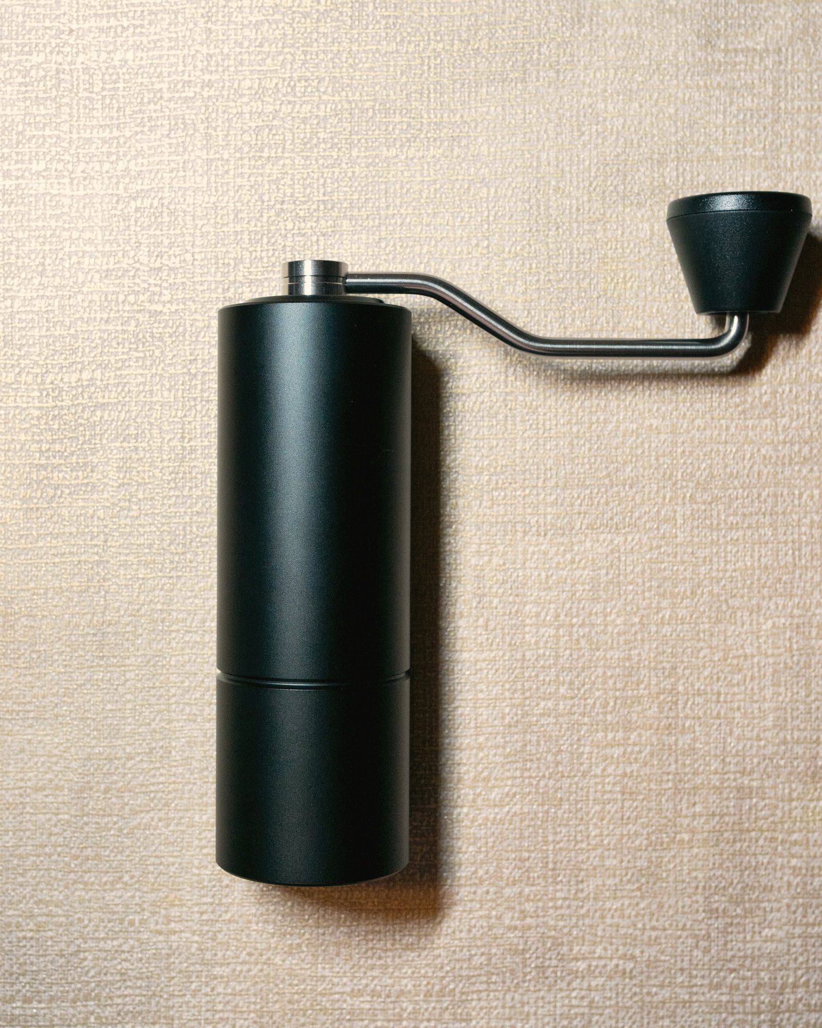 Molino de café manual negro mate sobre una superficie de lino claro