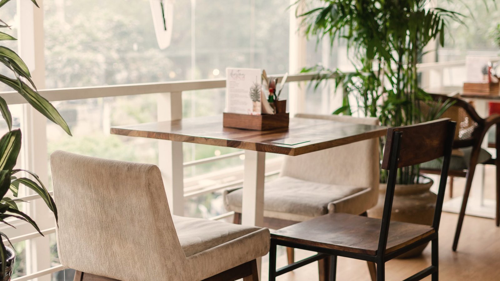 Interior luminoso del café: mesa de madera, sillas y plantas junto a la ventana